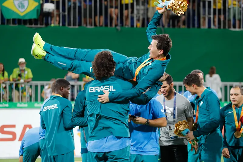 Ricardinho é erguido pelos colegas de equipe, de agasalho verde, com medalha no peito e um buquê dourado na mão.